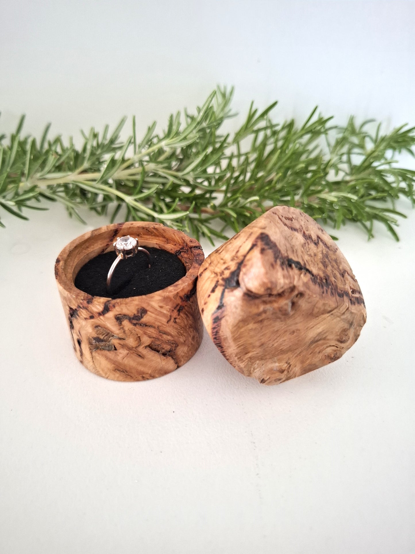 Wooden ring box with a ring inside, surrounded by greenery on a light background
