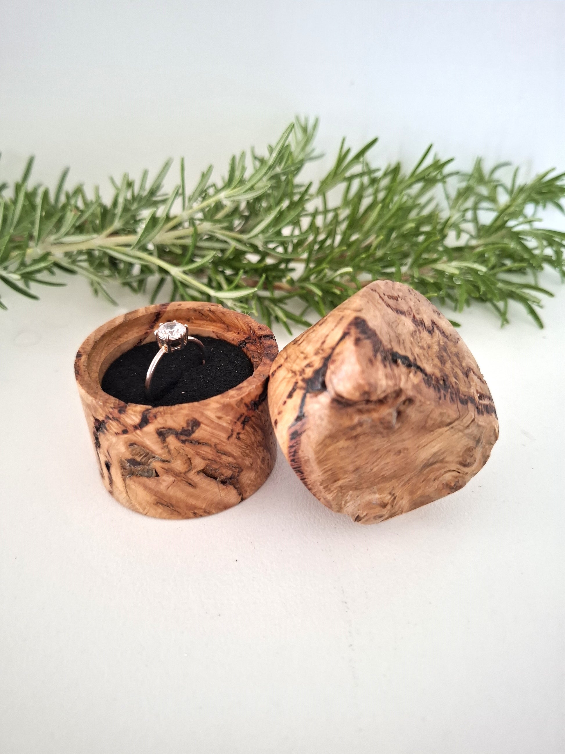 Wooden ring box with a ring inside, surrounded by greenery on a light background