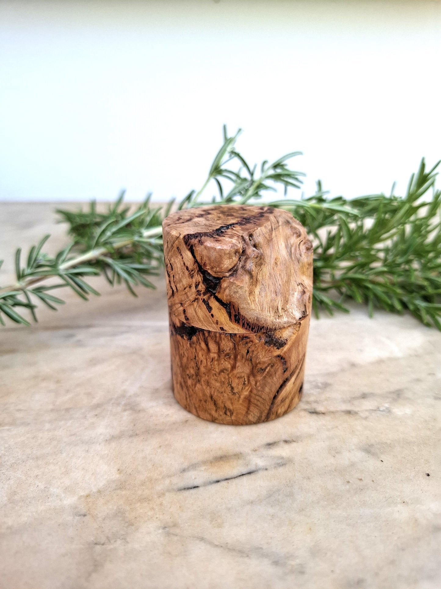 Wooden ring box with a ring inside, surrounded by greenery on a light background