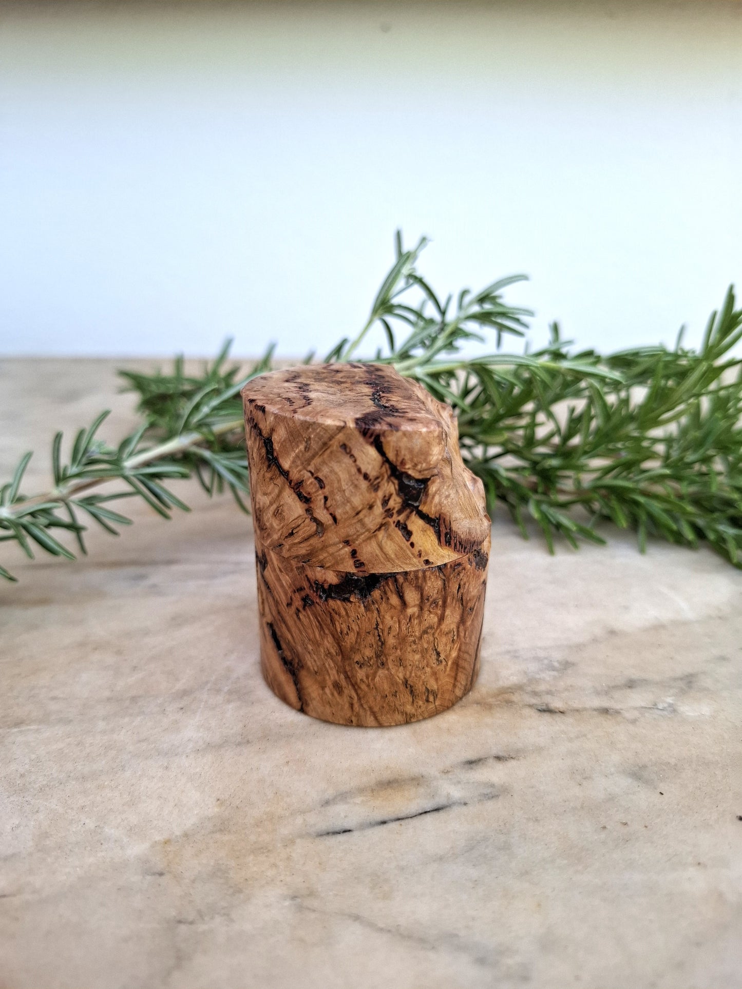 Wooden ring box with a ring inside, surrounded by greenery on a light background