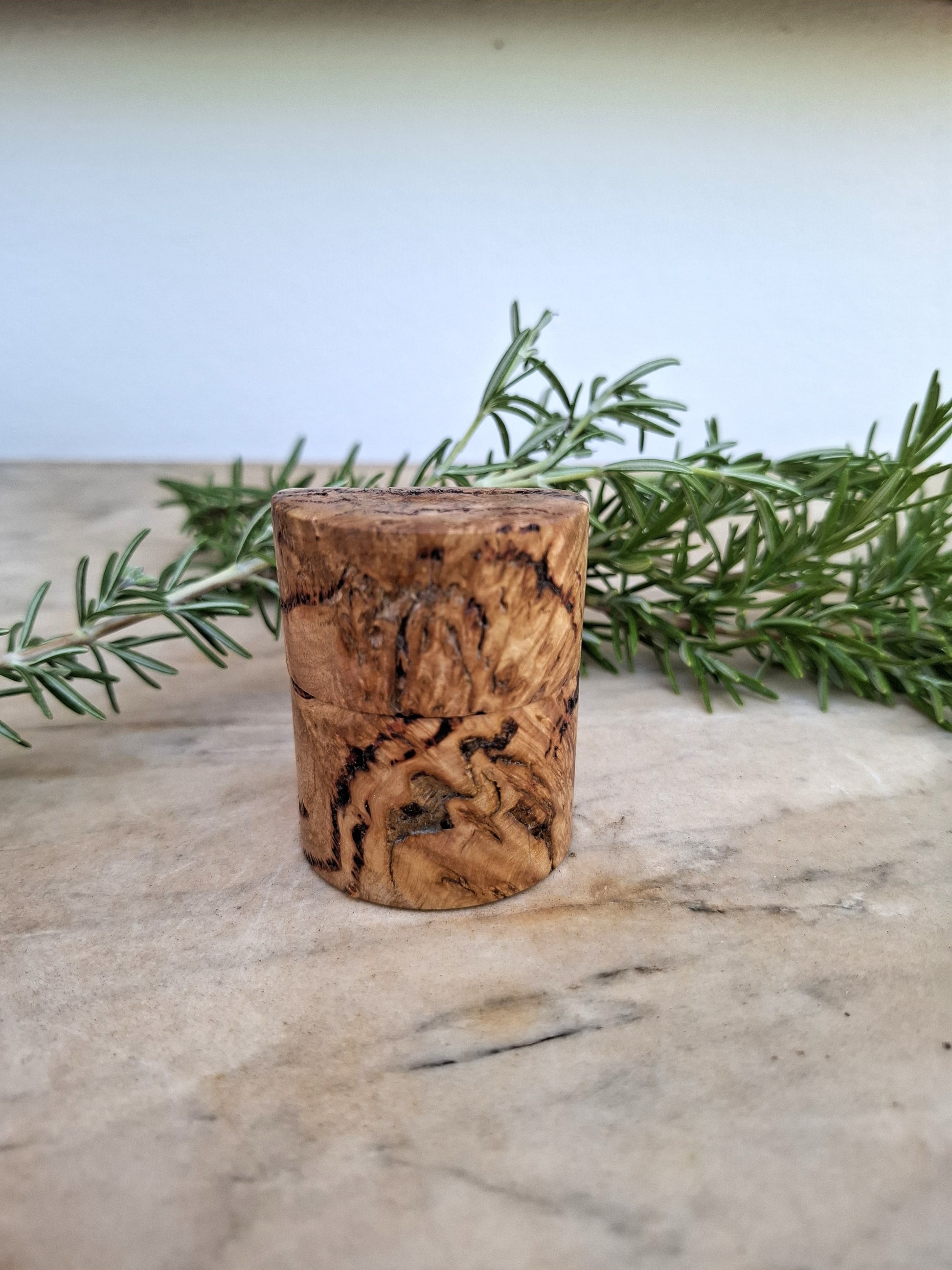 Wooden ring box with a ring inside, surrounded by greenery on a light background