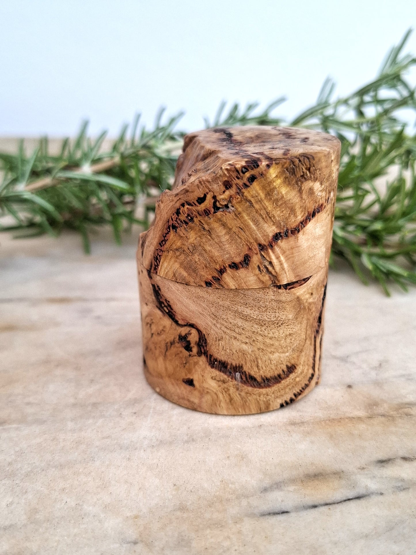 Wooden ring box with a ring inside, surrounded by greenery on a light background