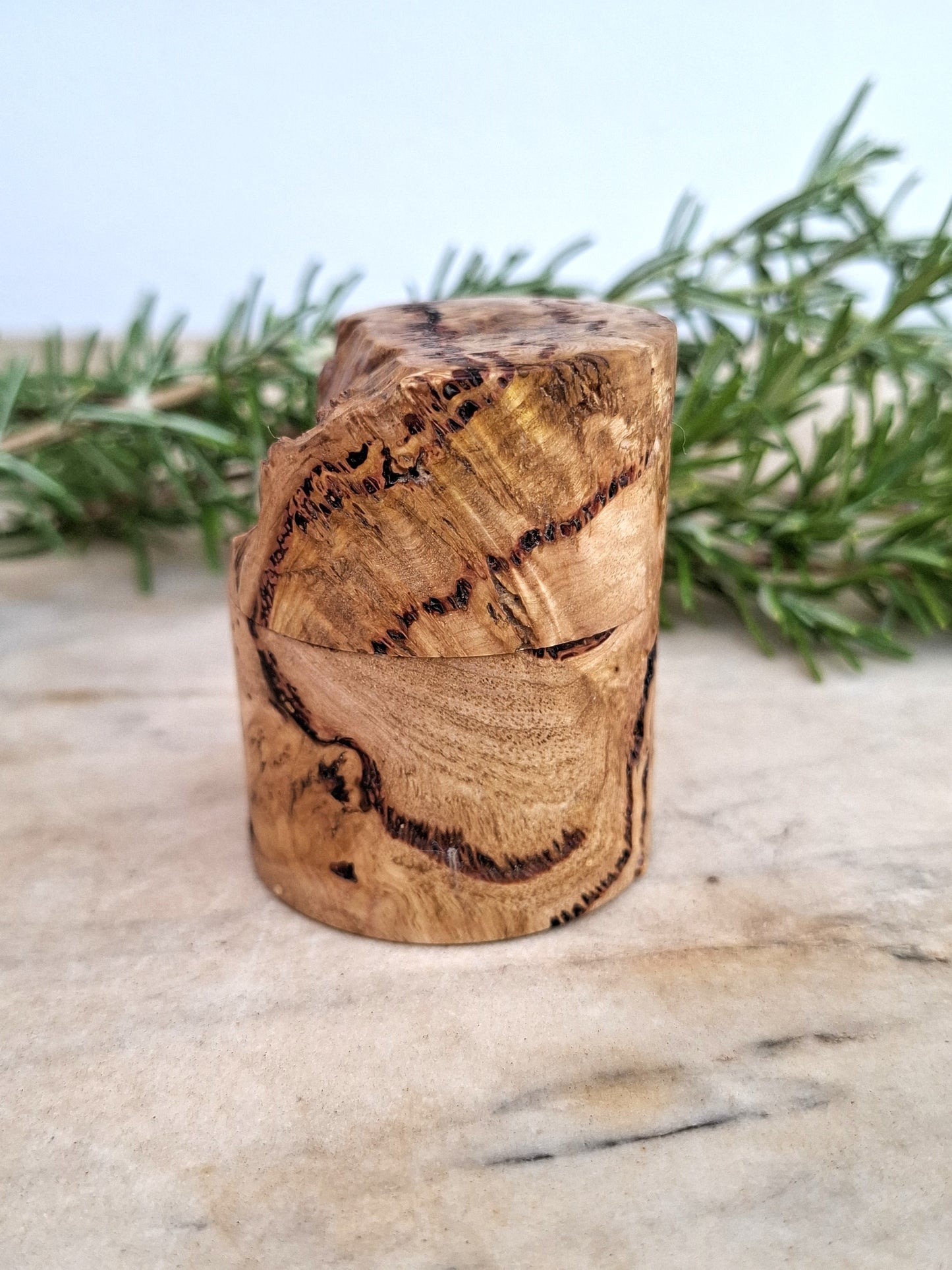 Wooden ring box with a ring inside, surrounded by greenery on a light background