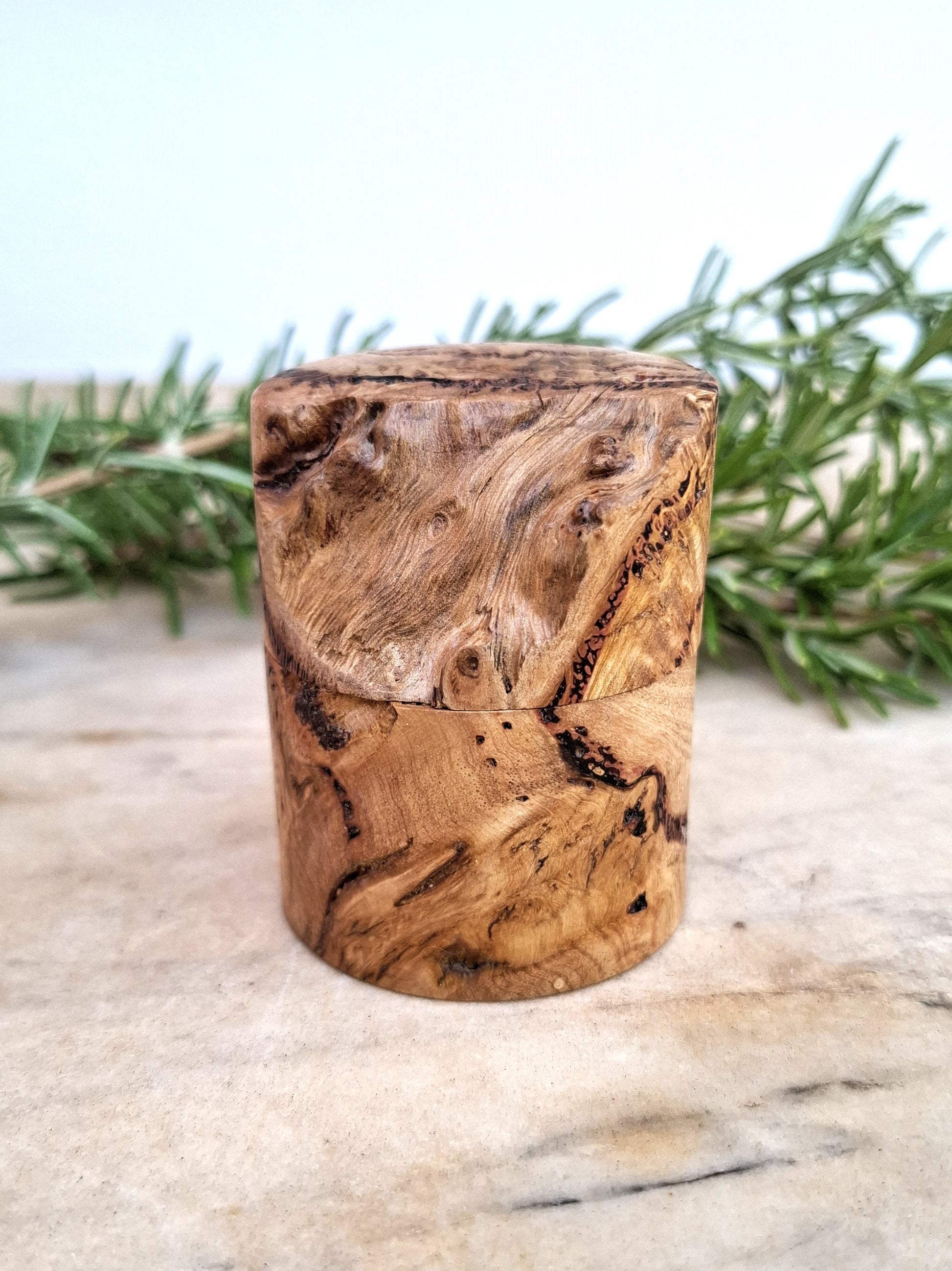 Wooden ring box with a ring inside, surrounded by greenery on a light background
