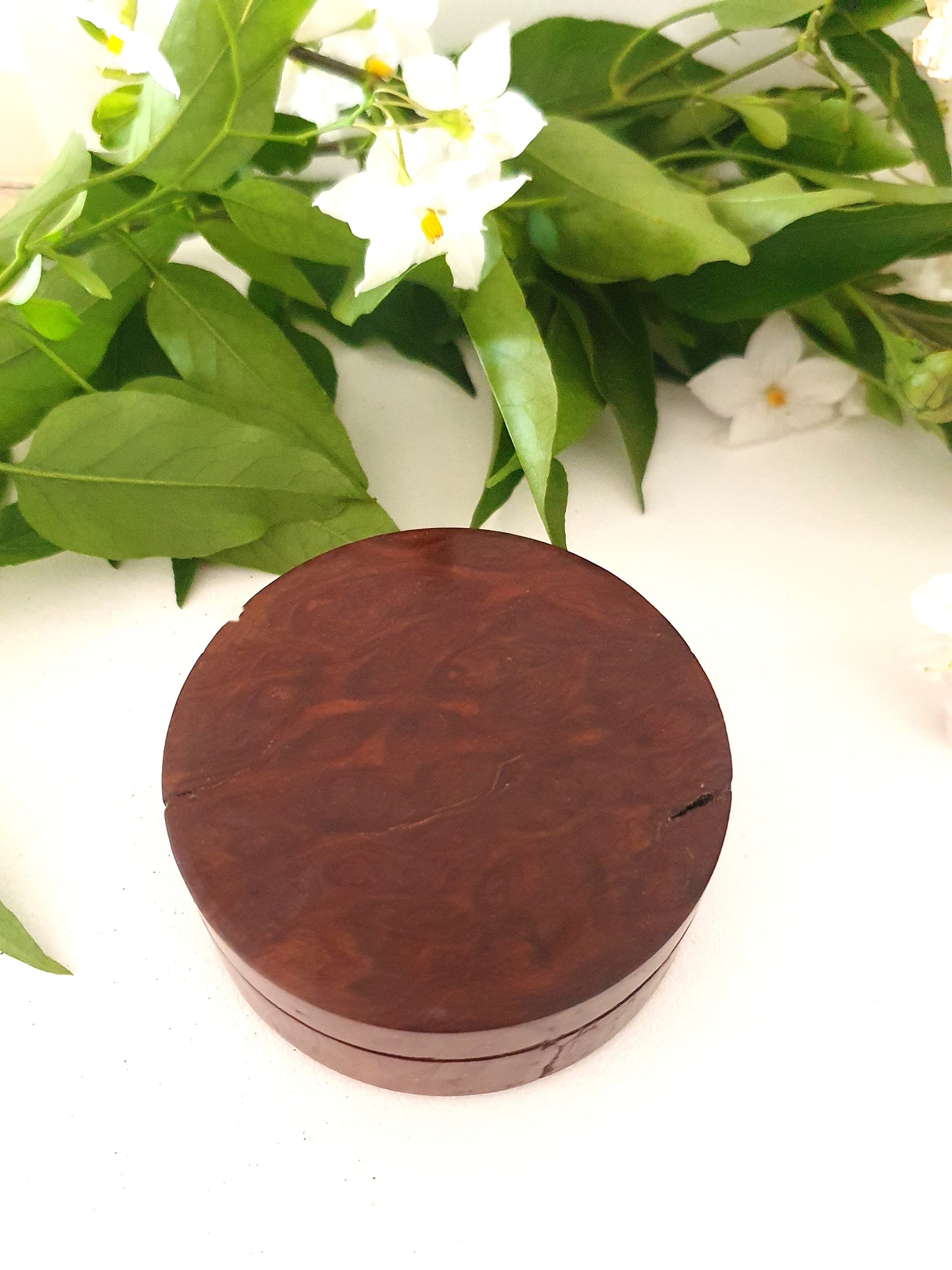 Wooden round box with a natural finish on a white background with green leaves and flowers.