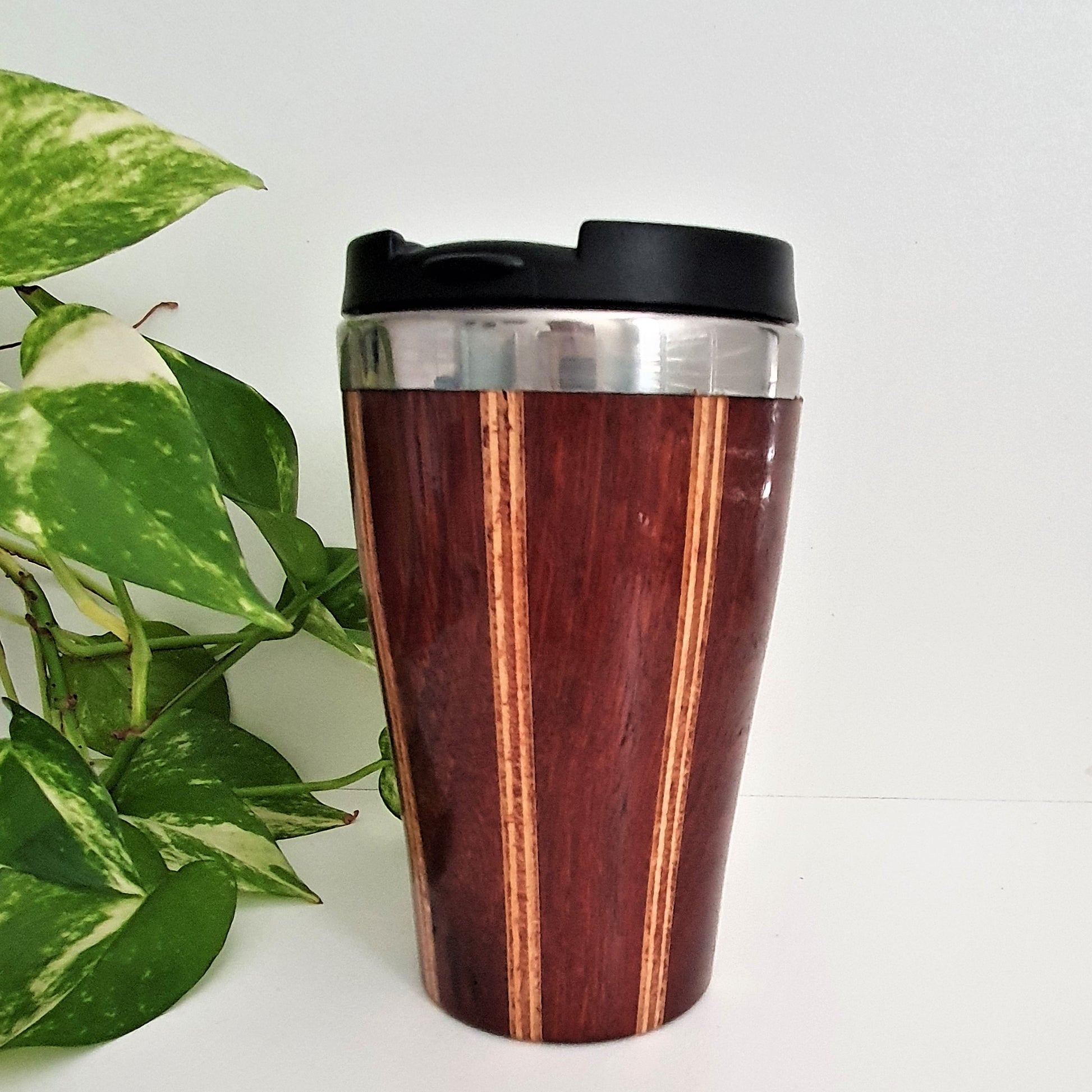 Wooden travel mug with black lid on a white background with green leaves.
