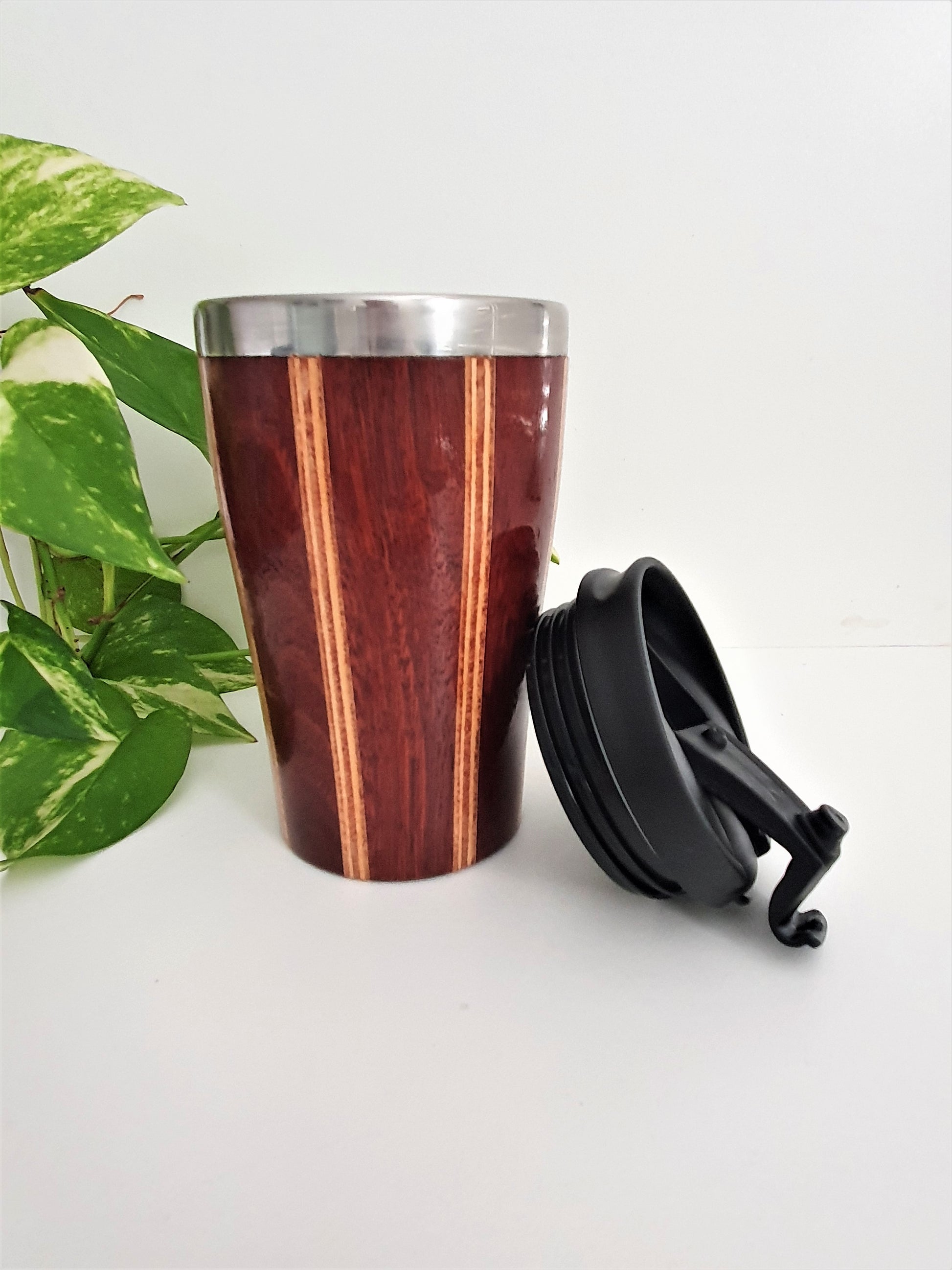 Wooden tumbler with black lid on a white surface with green leaves in the background