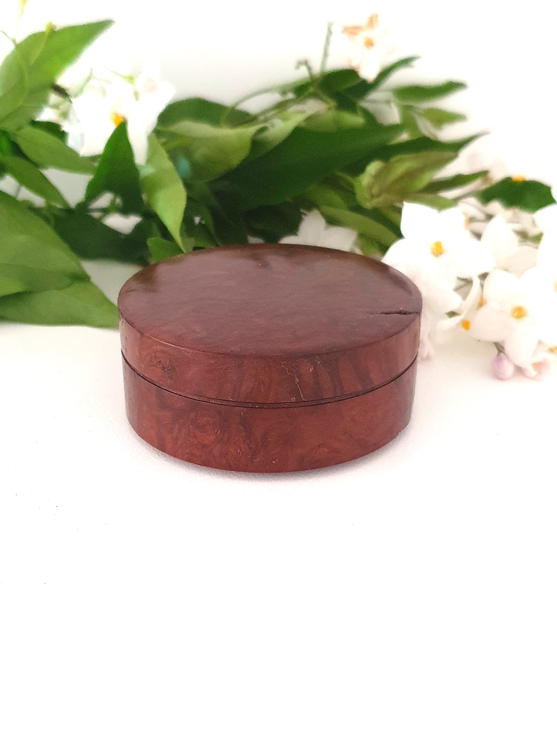Wooden round box with green leaves and white flowers in the background