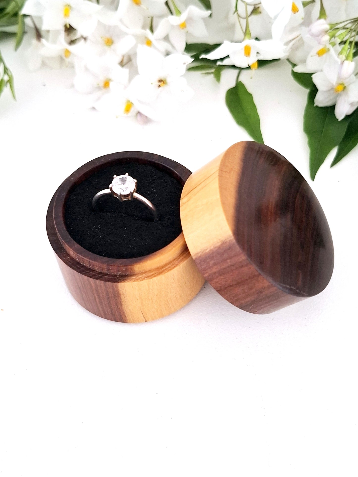 Wooden ring box with a ring inside, surrounded by white flowers on a light background