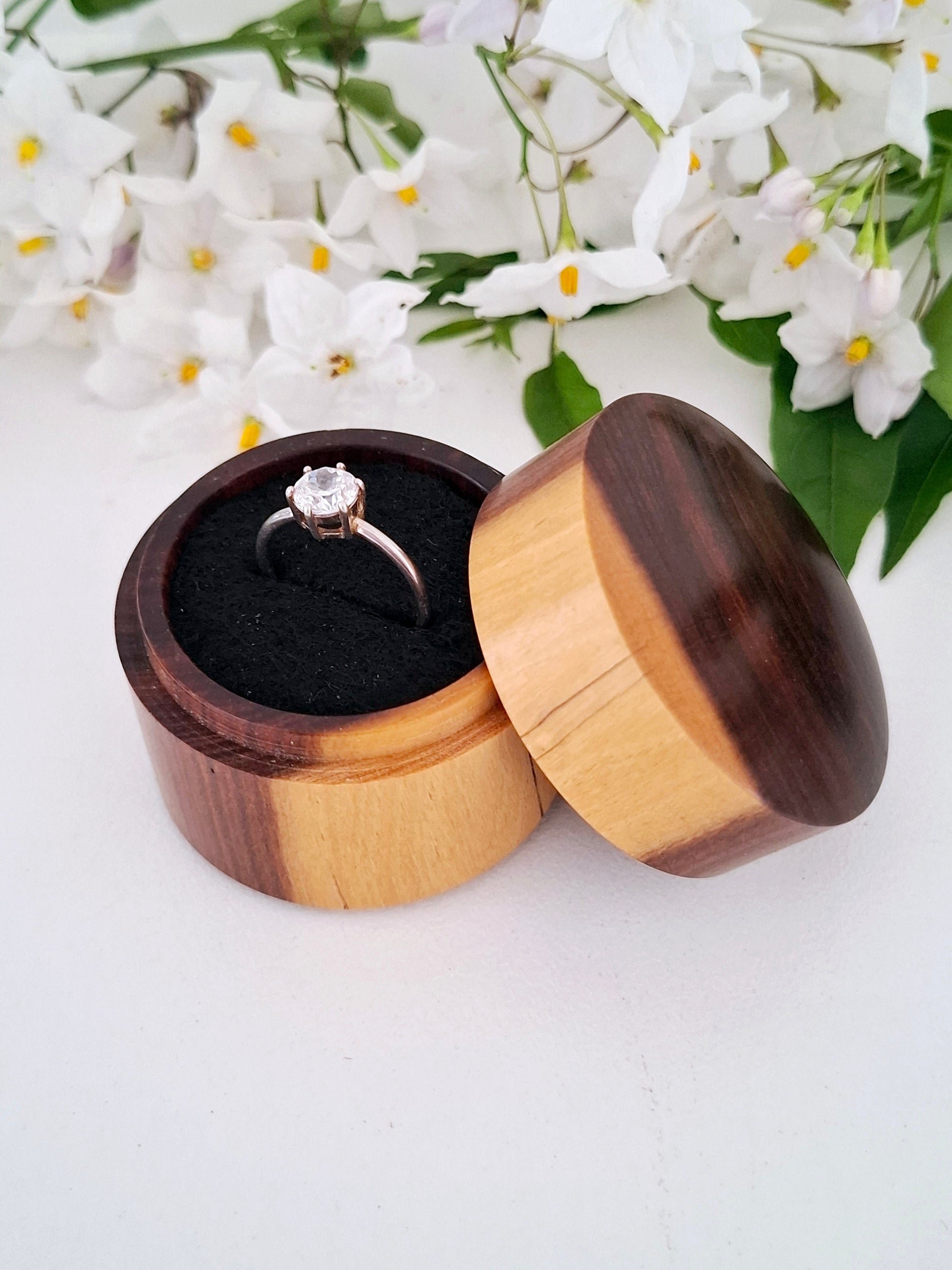Wooden ring box with a ring inside, surrounded by white flowers on a light background