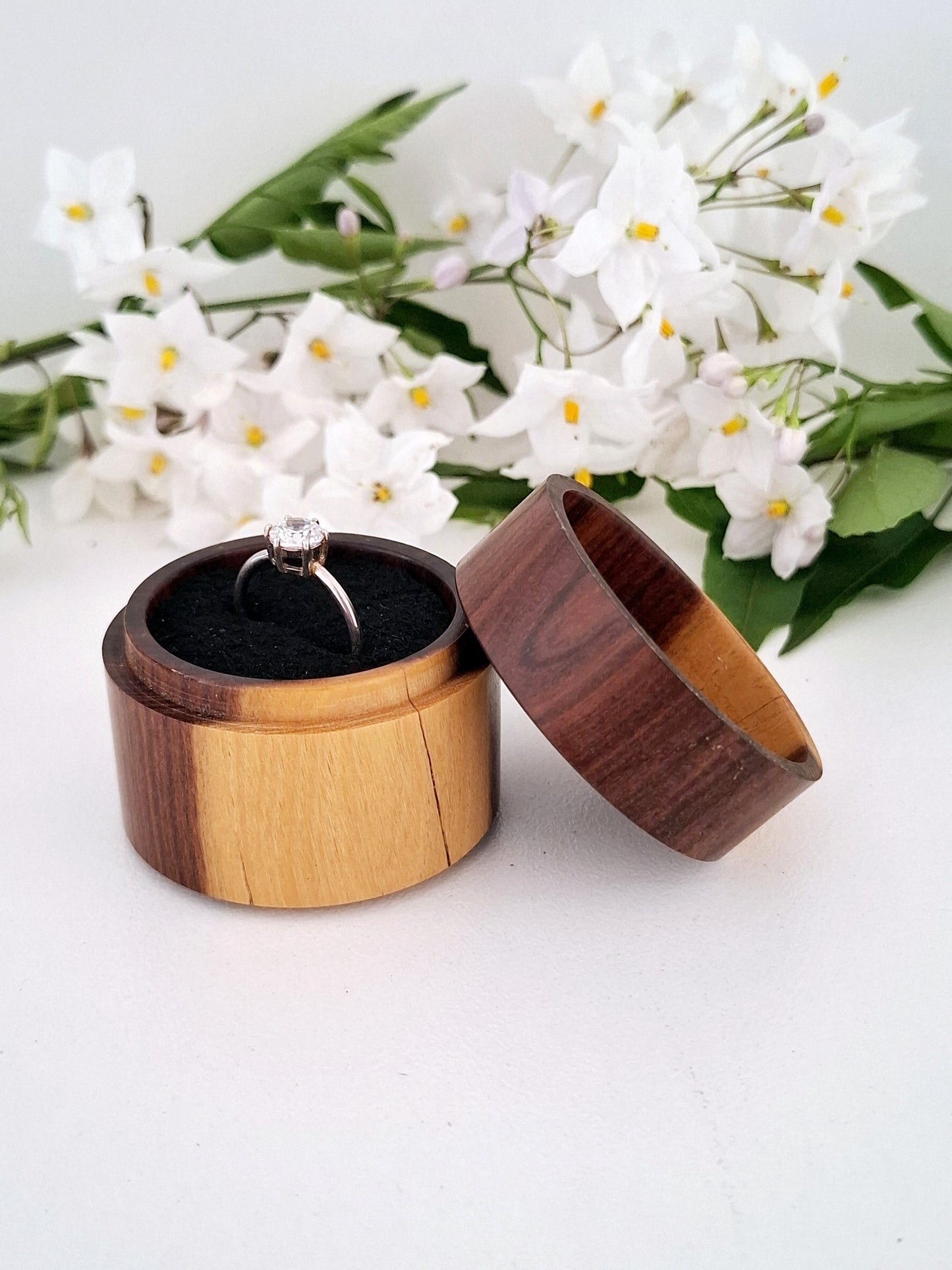 Wooden ring box with a ring inside, surrounded by white flowers on a light background