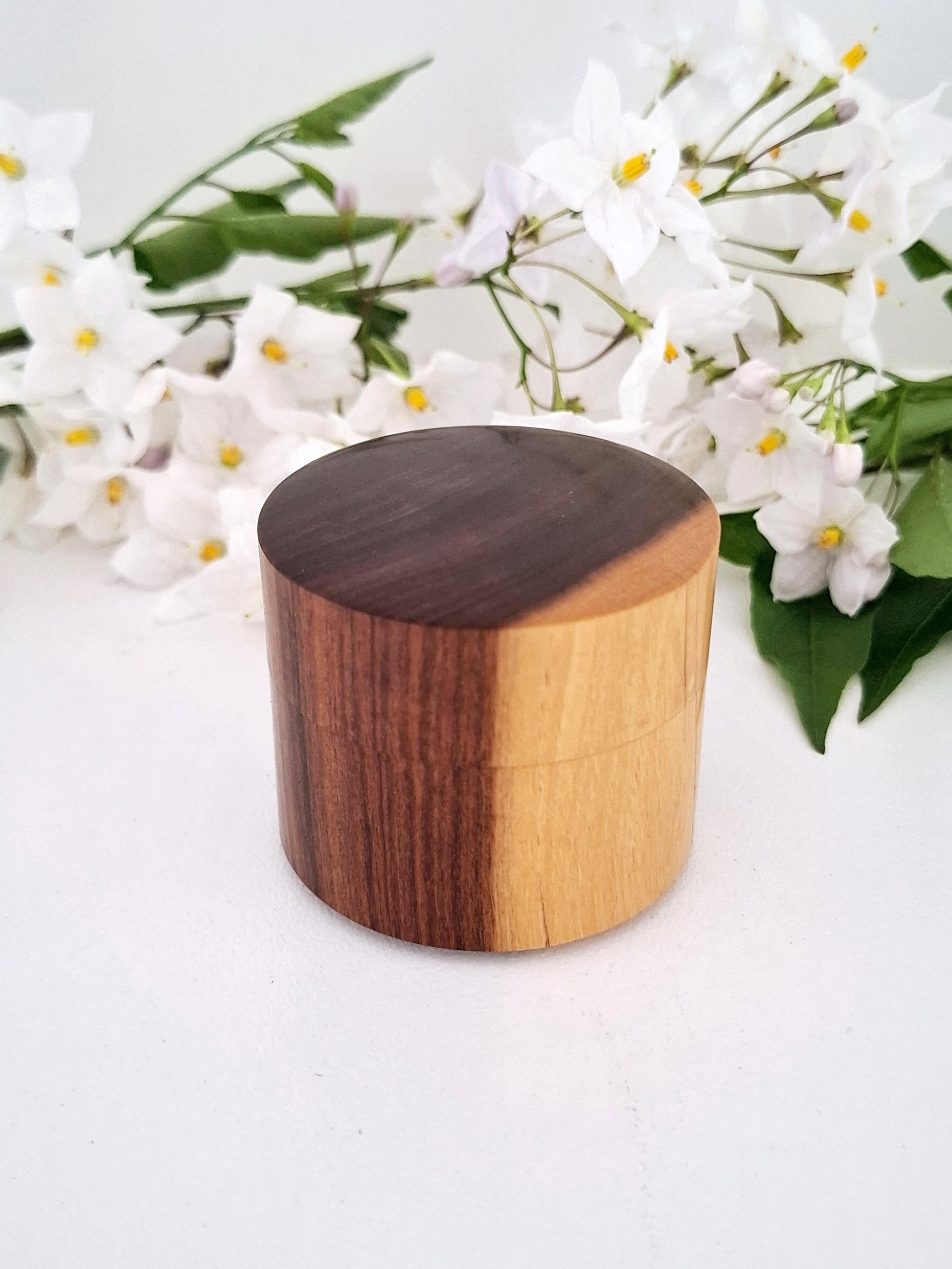 Wooden cylindrical ring box with two-tone finish on a white background with flowers.
