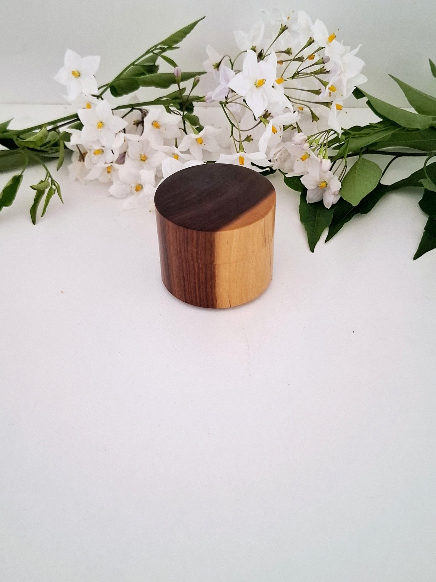 Wooden cylindrical ring box with a white flower arrangement on a light background